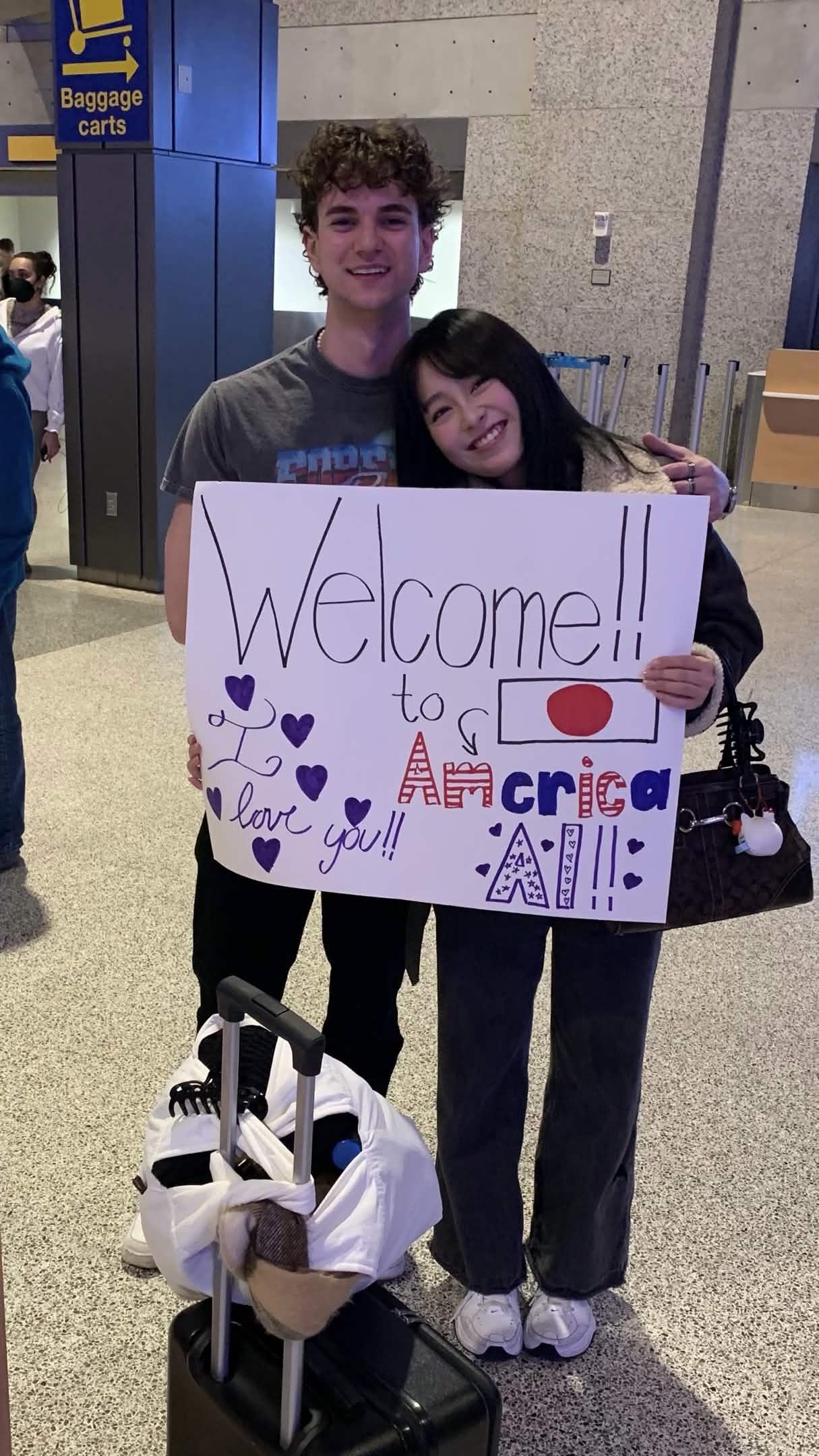 Ai and Austin at the airport with a handmade Welcome to America sign for Ai.