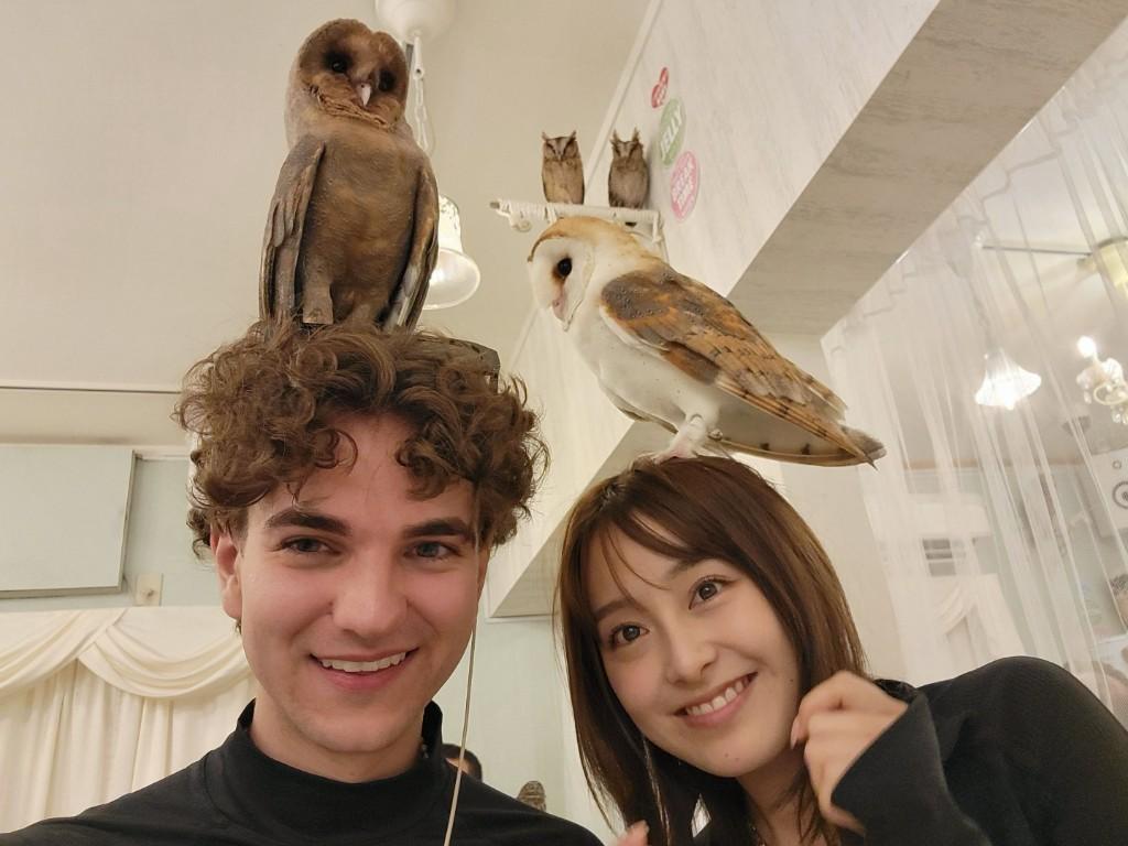 Ai and Austin smiling at an owl café in Tokyo, each with an owl perched on their head.